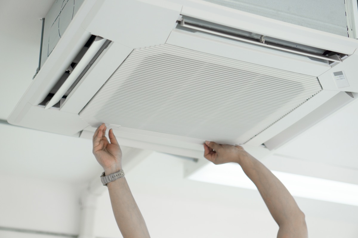 A hand of a man trying to maintenance filter of air conditioner in the room.