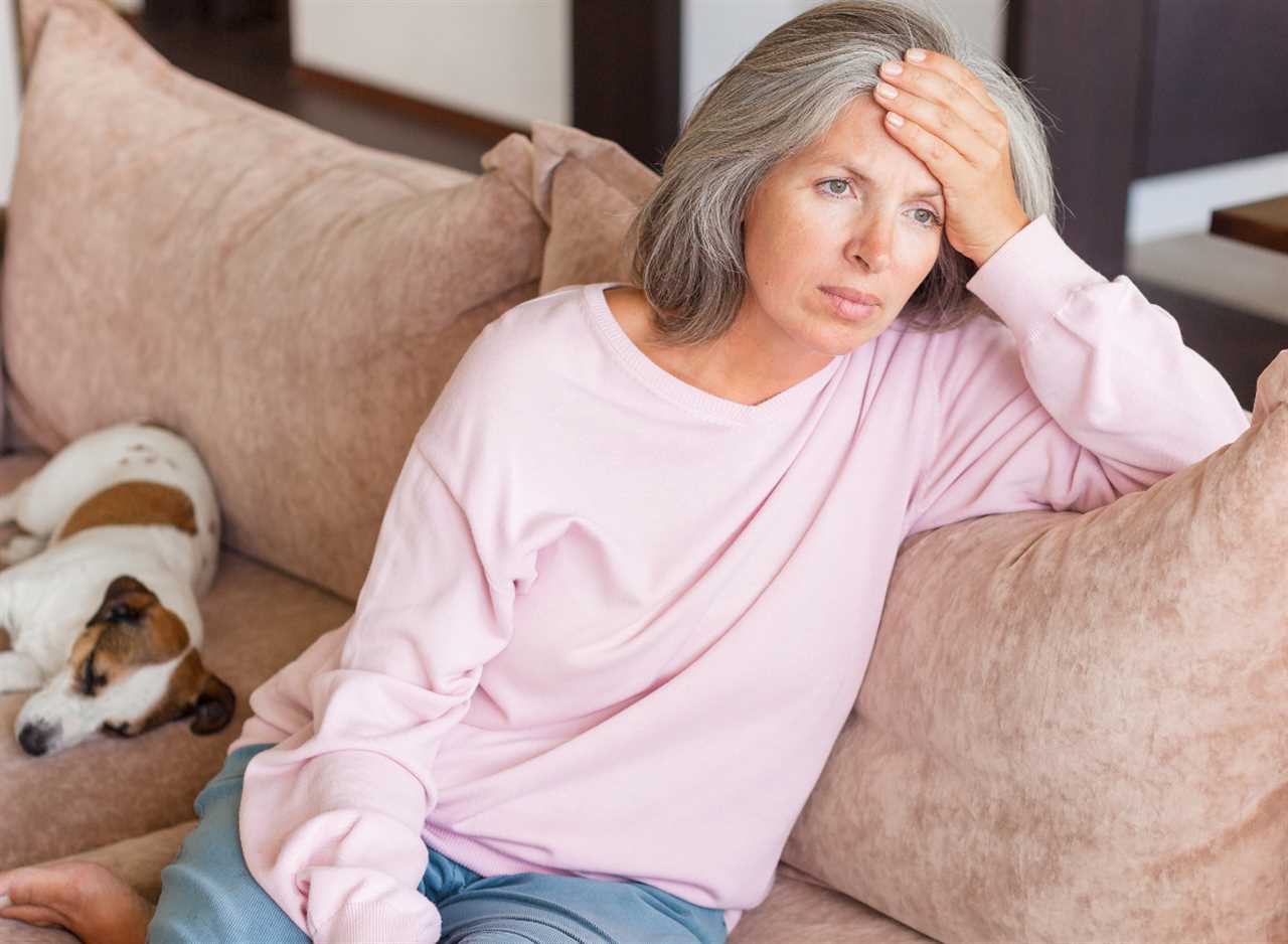 unhappy woman sits on couch, hand on forehead