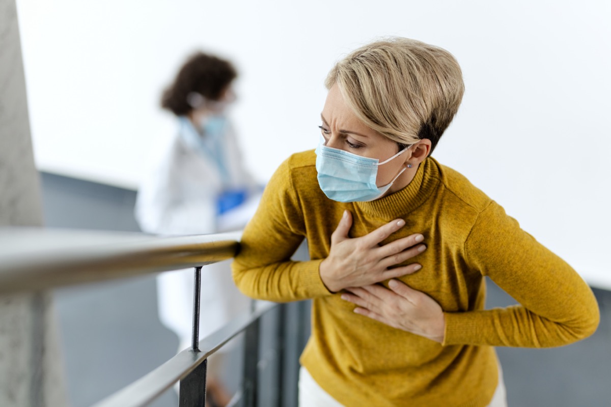 Sick woman feeling chest pain and wearing face mask in a lobby at medical clinic.