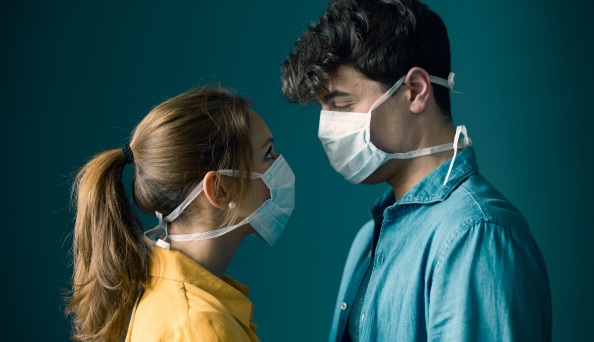 Young romantic loving couple wearing a protective face mask and staring at each other's eyes, pandemic and feelings concept