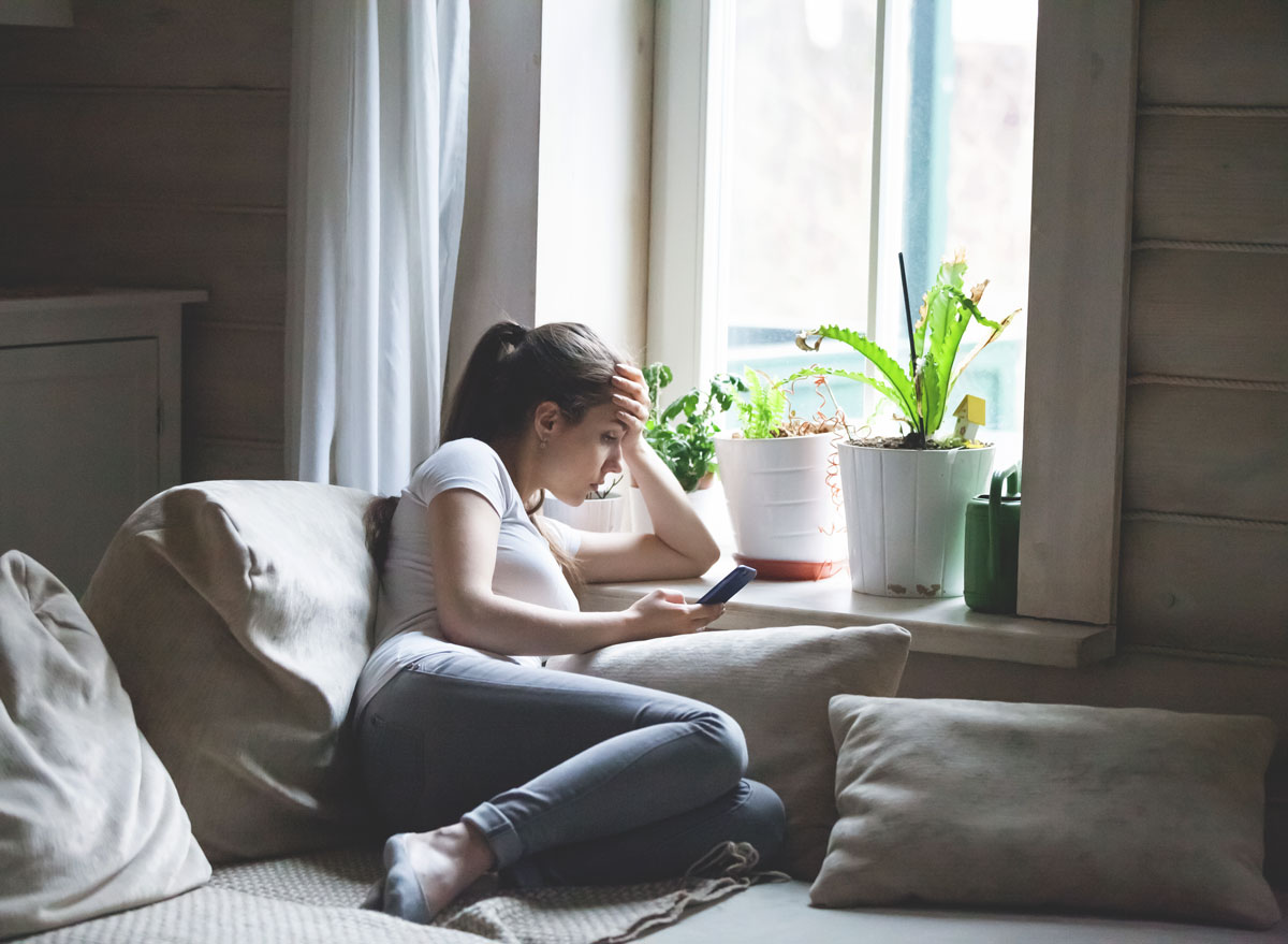 Woman sitting on bed looking at phone bored and in a bad mood