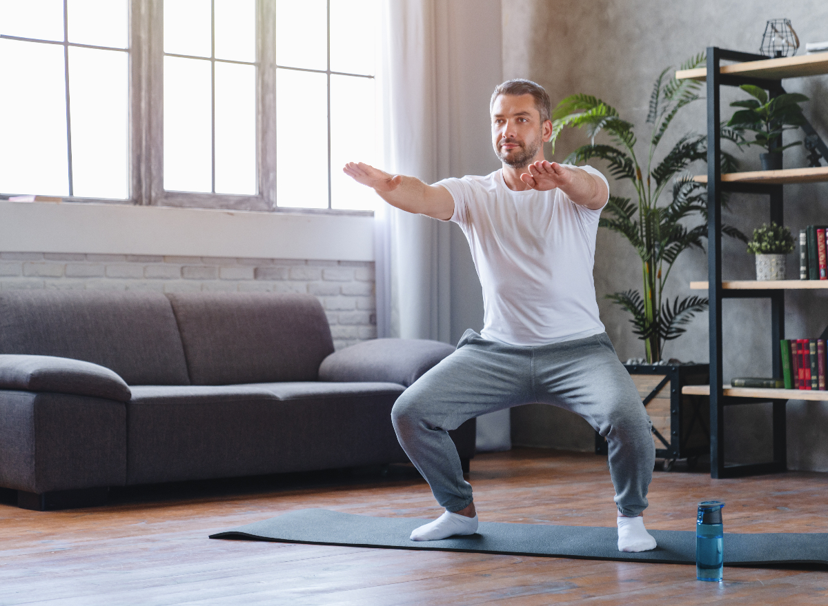 man in his 50s does squat on yoga mat