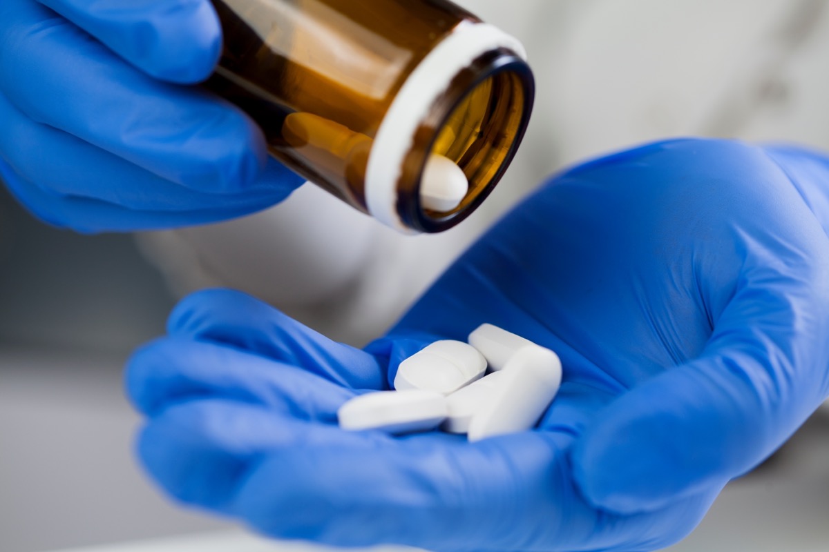 Closeup of medical worker or pharmacist hands wearing blue latex protective gloves,pouring white medicine pills on palm of hand.