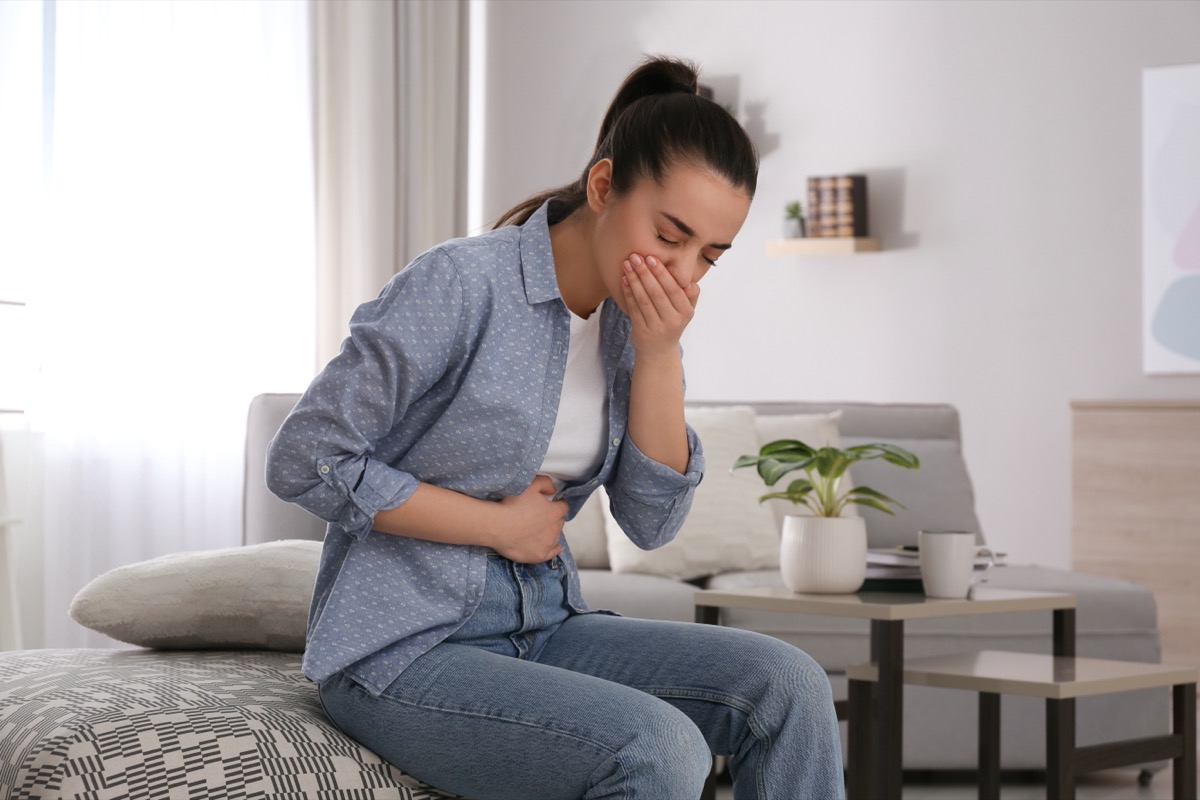 young woman with nausea in all denim outfit sitting on bed