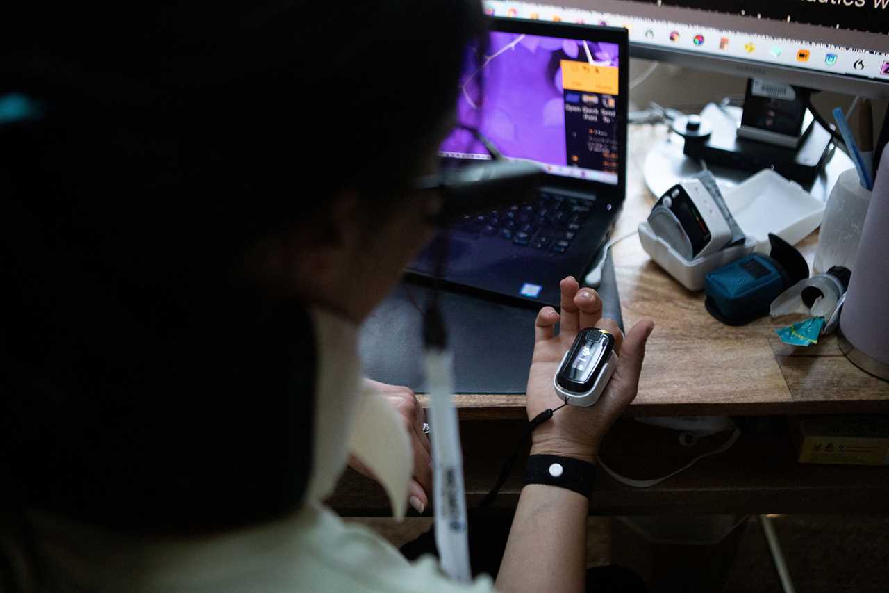 Lauren Nichols, who has long COVID, takes a break from work to read her blood oxygen levels and heart rate from a machine on her finger in her home in Andover, MA, on Aug. 3, 2022.