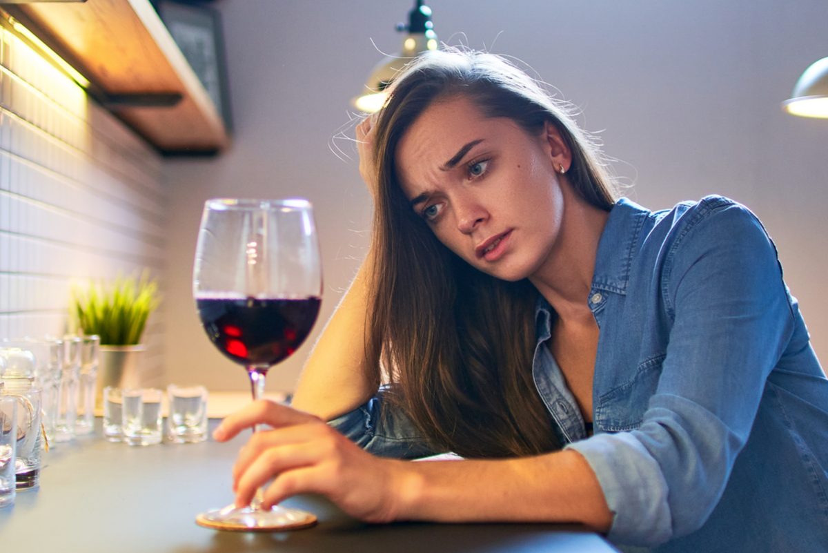 Sad woman drinking wine at kitchen.