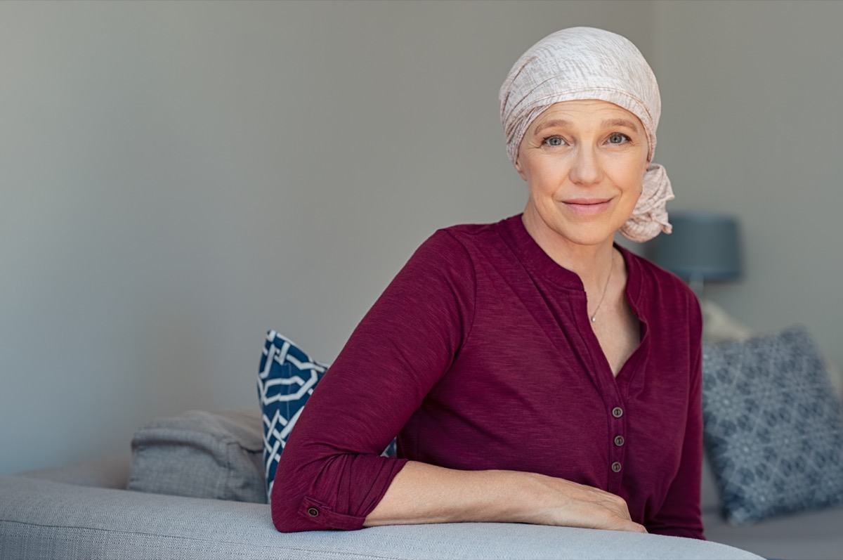 Mature woman with cancer in pink headscarf smiling sitting on couch at home