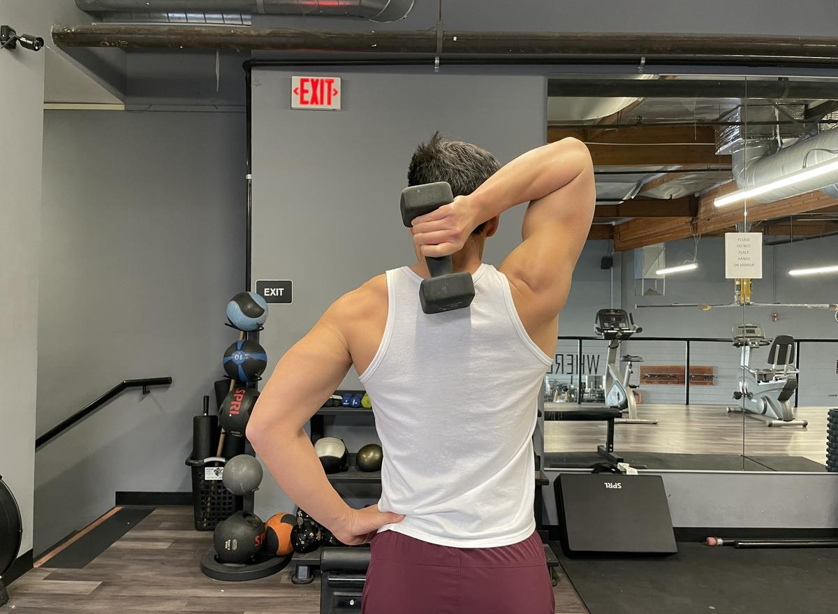 trainer demonstrating overhead triceps extension to get rid of bat wings