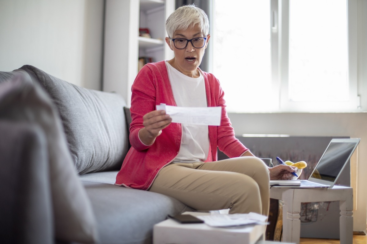 Surprised senior mature woman counting bills at home.