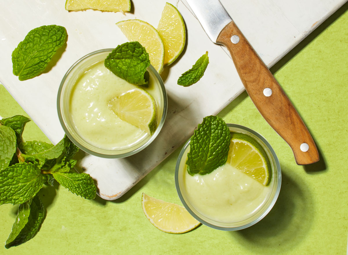 avocado lime smoothie on a white cutting board with limes and a knife on a green table