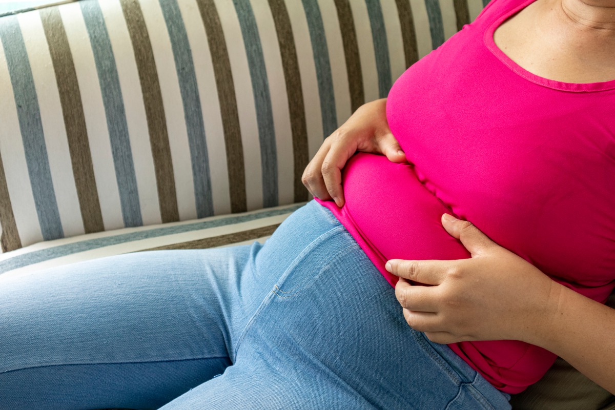 Woman shows excess fat of the waist while sitting on her sofa.