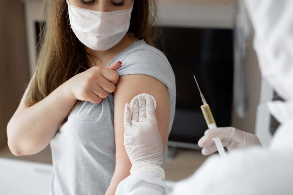 Doctor in personal protective suit or PPE inject vaccine shot to stimulating immunity of woman patient at risk of coronavirus infection.