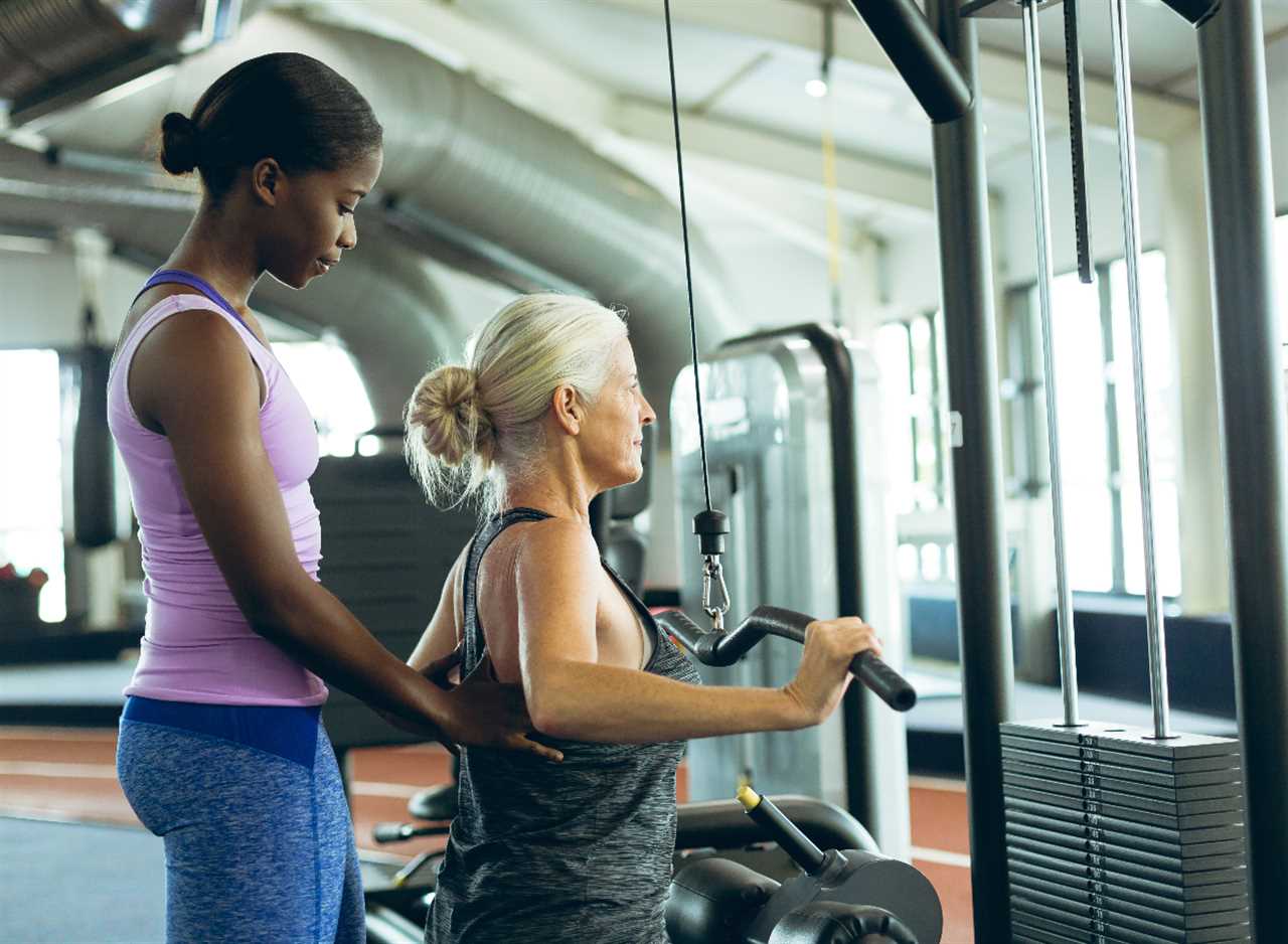 mature woman doing lat pulldown with her trainer, exercise to reverse aging after 60