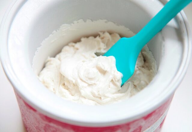 Vanilla ice cream in an ice cream maker with a blue spatula.