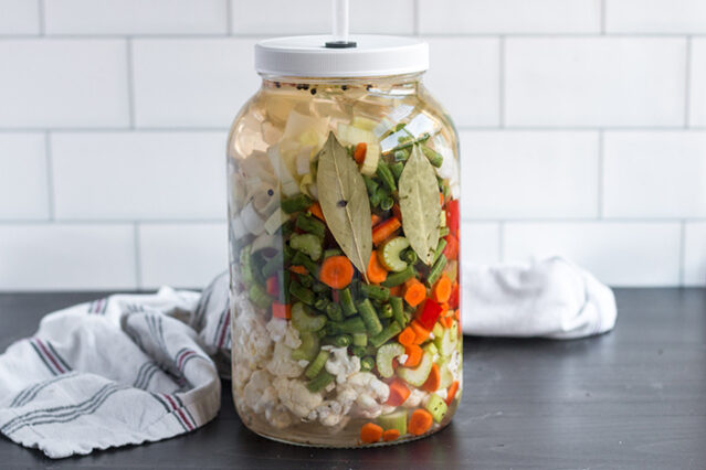 Large jar of giardiniera against a white tile background.