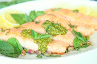 Salmon fillets topped with bright green pistachio pesto on a white platter.