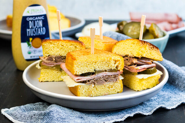 Cuban sandwiches on a white plate, skewered with cocktail toothpicks, Primal Kitchen Dijon Mustard in the background.