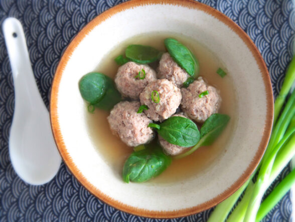 Overhead shot of wonton meatballs in broth with spinach, green onions, white spoon.