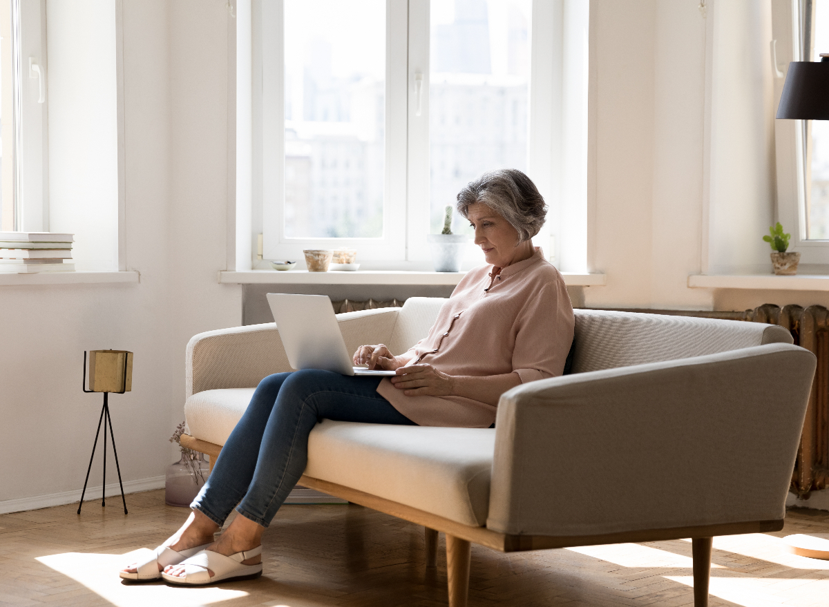 mature woman on laptop sedentary at 60 on the couch