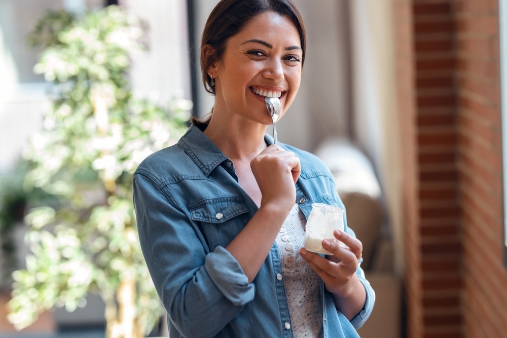 A smiling woman eating yogurt with a spoon.