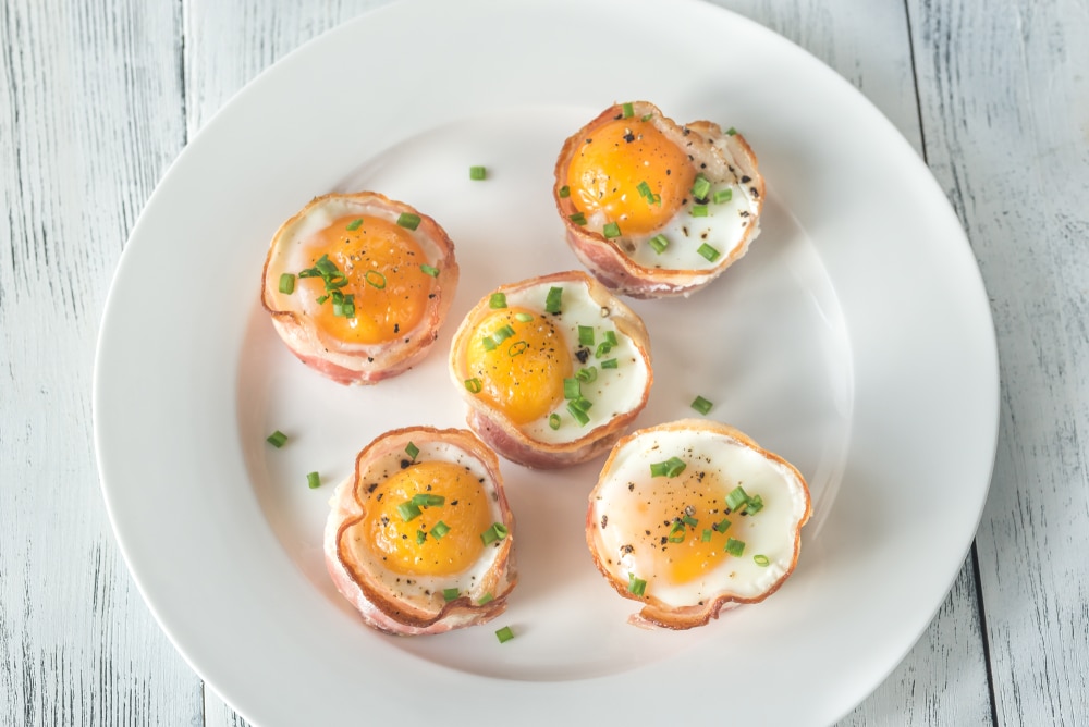 Bacon and egg cups on a white plate.