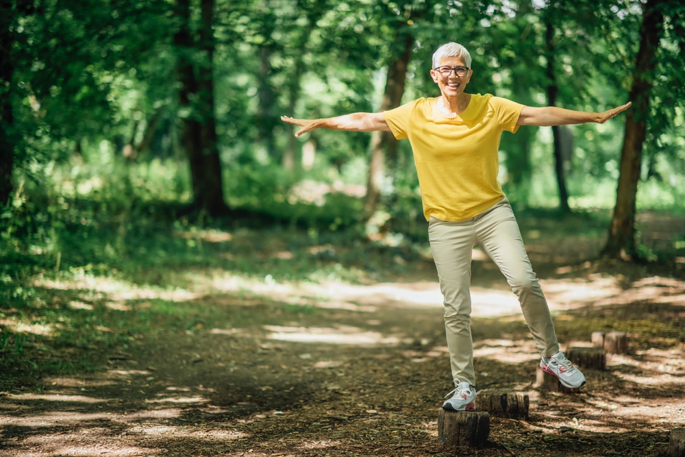 Happy older woman balancing on logs in the woods.