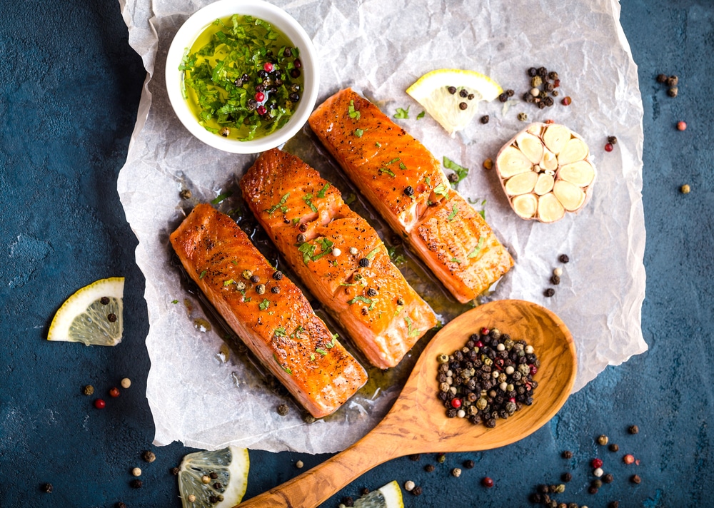 Overhead view of cooked salmon filets and seasonings on a blue rustic concrete background.