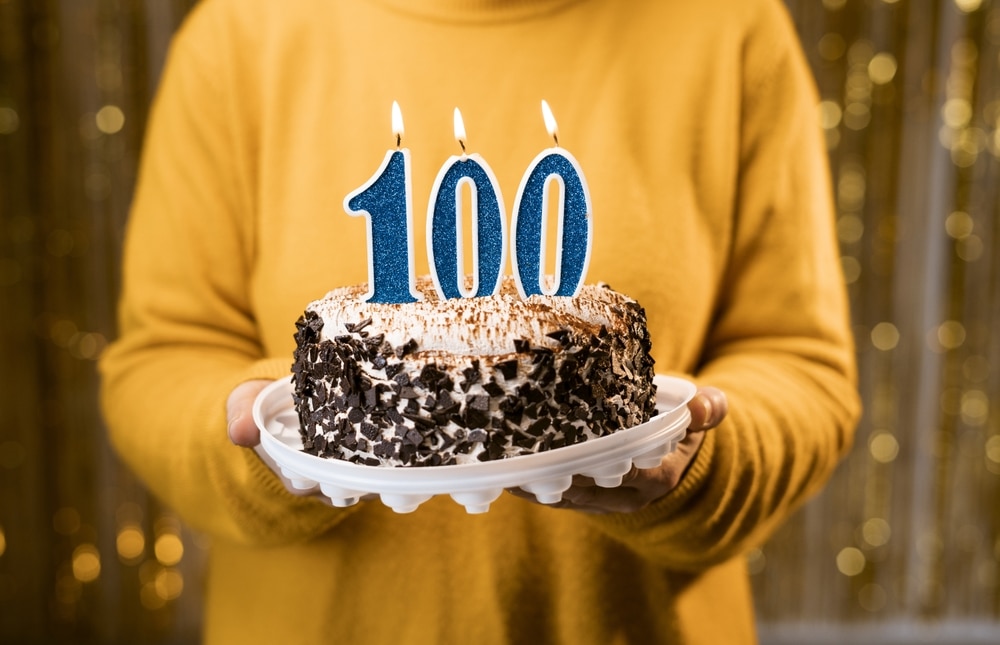 Woman holding a birthday cake with candles that say 100.