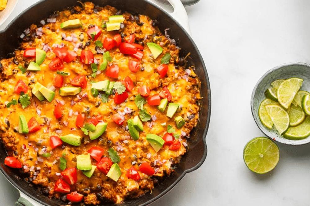 Overhead view of healthy chili cheese dip in a skillet next to a bowl of lime wedges.