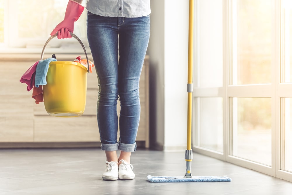 Woman in gloves holding a mop bucket in the kitchen.