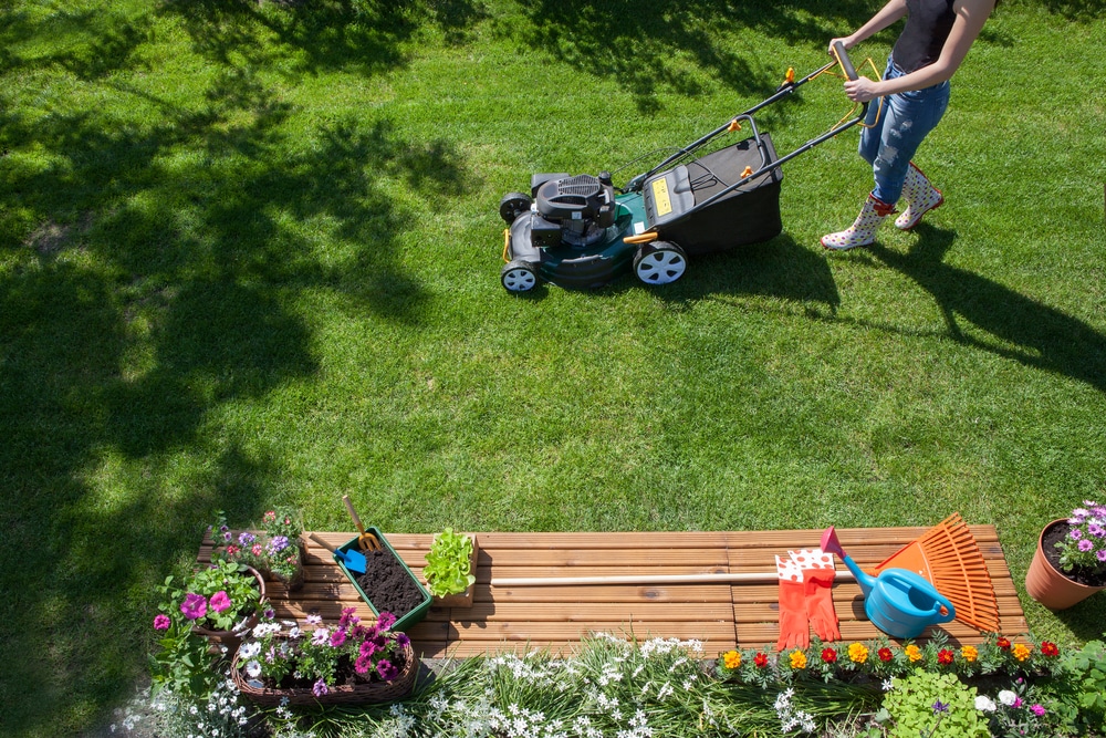 A woman pushing a lawnmower across a green a lawn.