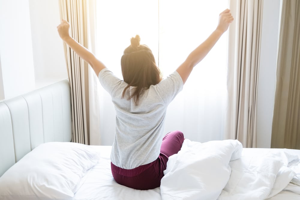 woman waking up to morning sunshine through curtains