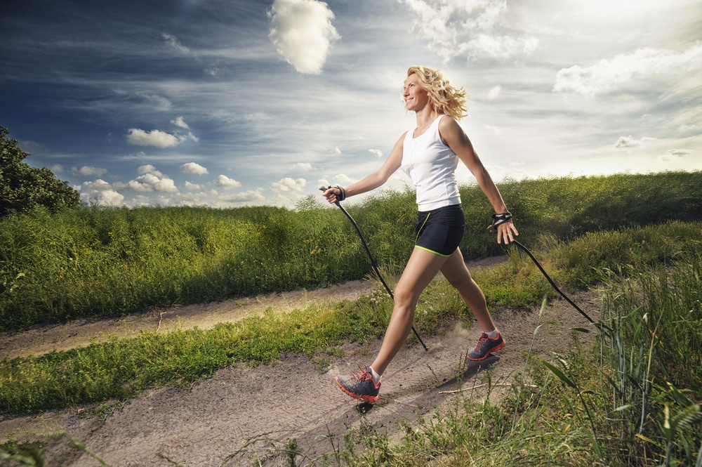 A woman nordic walking outdoors with trekking poles.