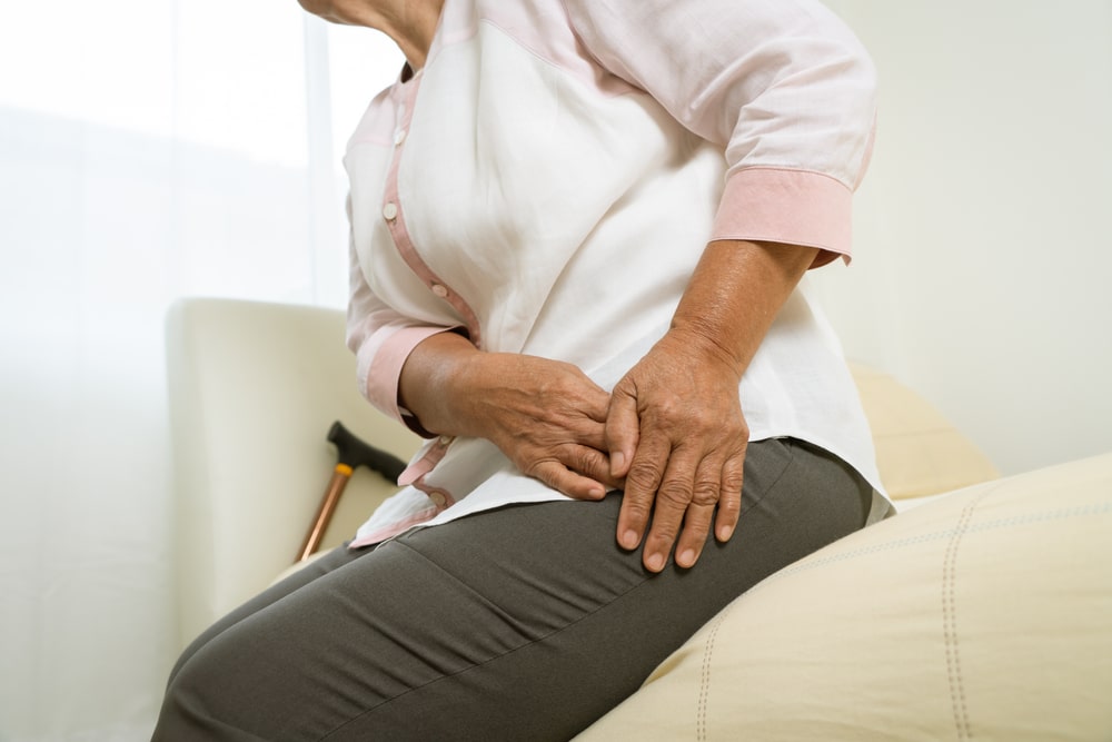 An older woman massaging hip pain while sitting on a bed.