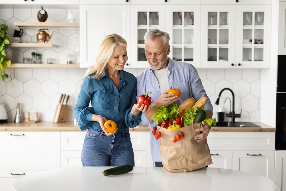 Happy older couple unpacking a bag of groceries in the kitchen.