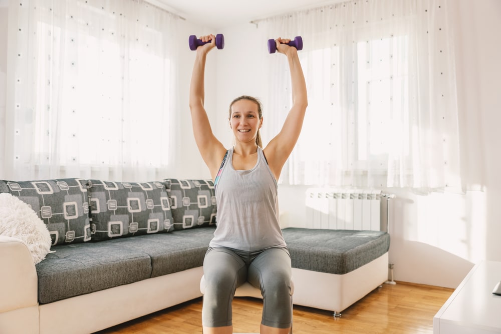 A woman sitting in a chair doing overhead presses with small dumbbells.