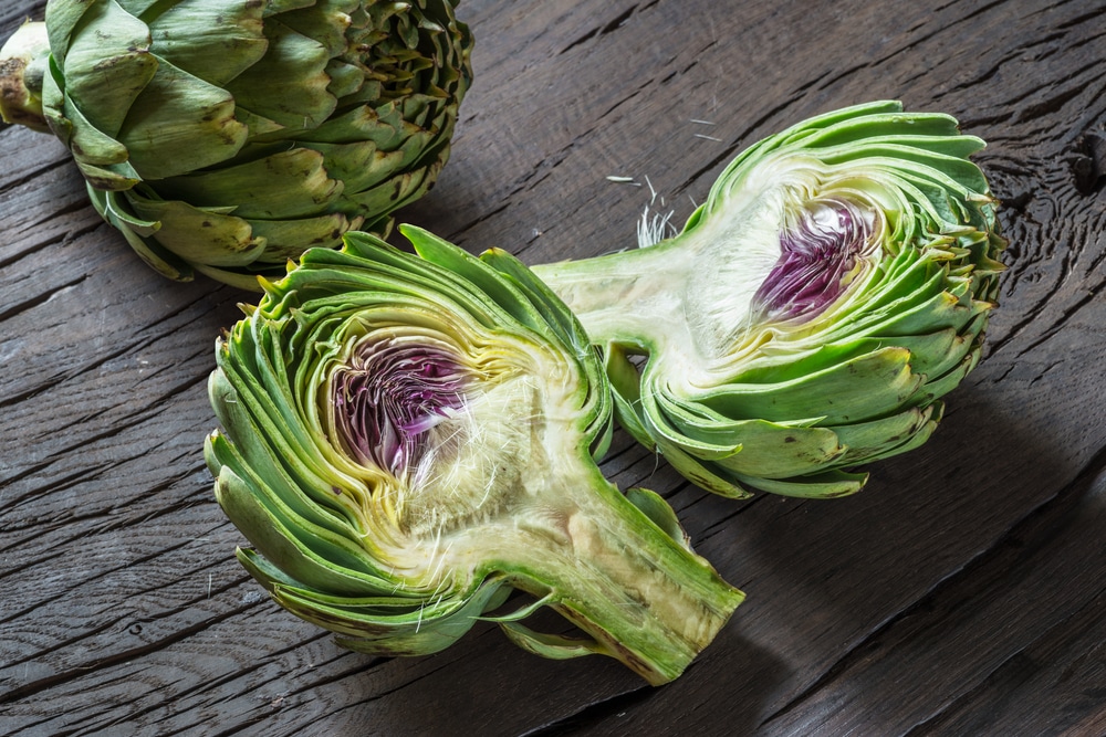 Green and purple artichoke cut in half on a wooden table.