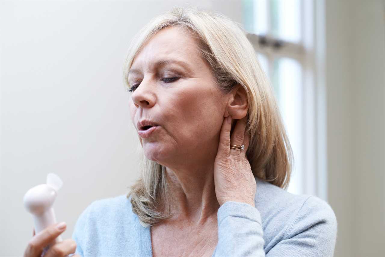 Woman experiencing hot flash using a small fan.