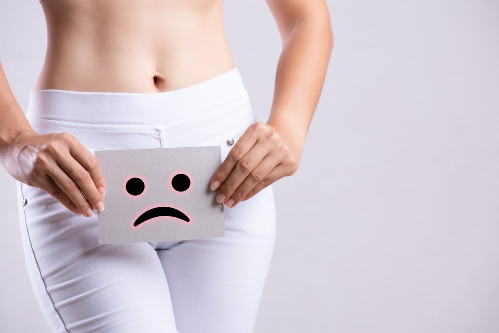 Woman holding a picture of a sad face over her pelvic region.